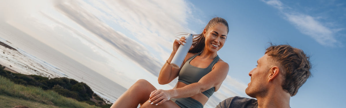 Two athletes sitting on a coastal headland, one holding a Rare Forms bottle