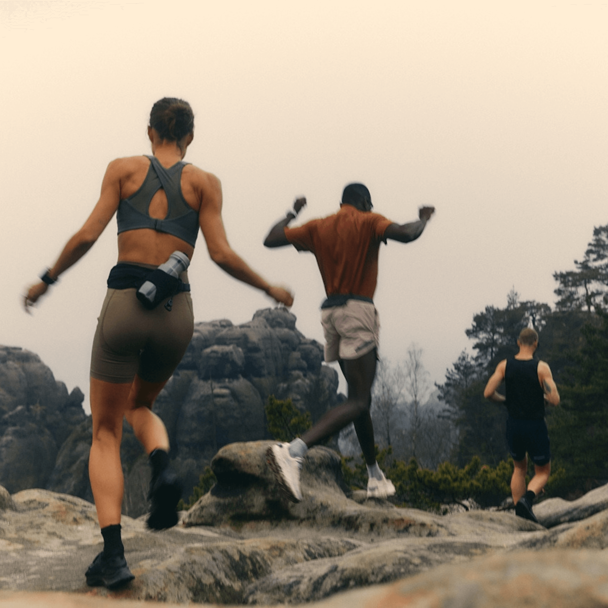 Three people running on a rocky trail with a mountainous background.